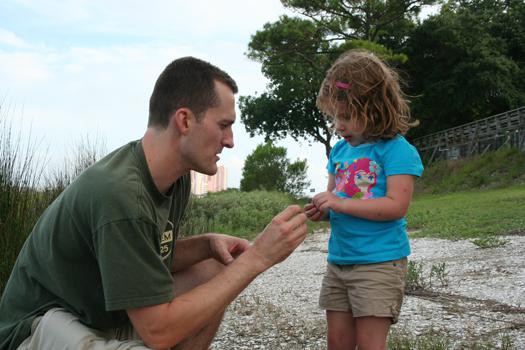 An adult and a young girl examine a small object outdoors