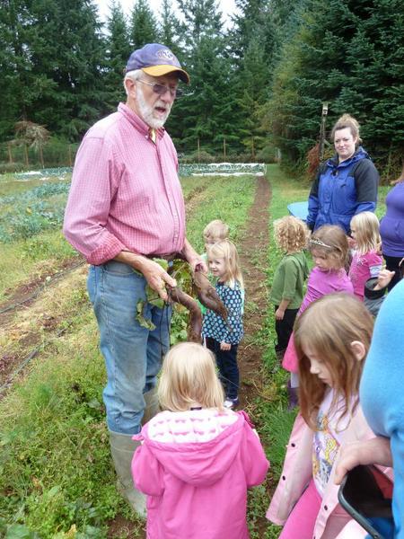 An adult shows harvested plants to a small group of children