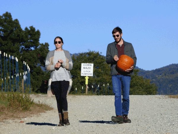 A woman and a man carrying a pumpkin at an agritourism farm