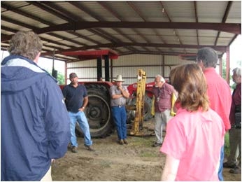 Farmer and others stand in a circle discussing near tractor