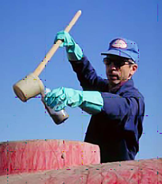 Photo of person dipping a sludge sample from top of tanker