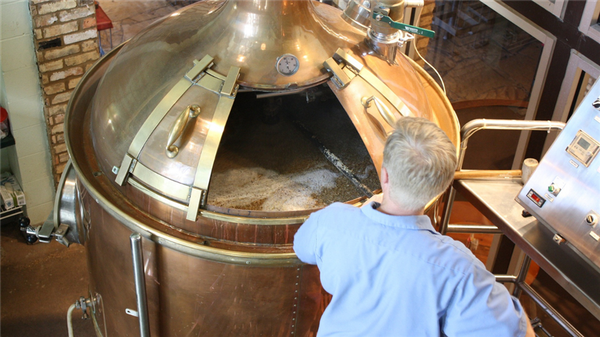 Photo of distillery employee stirring mash in a copper container