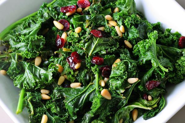 Photo of kale with pine nuts and cranberries in a bowl.
