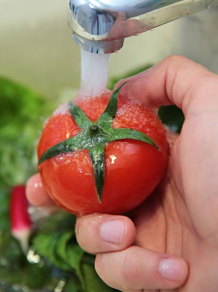 Photo of a tomato being washed under a faucet.