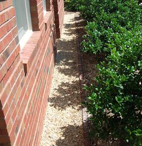 Photo of a gravel border between a brick exterior of a house and bushes.