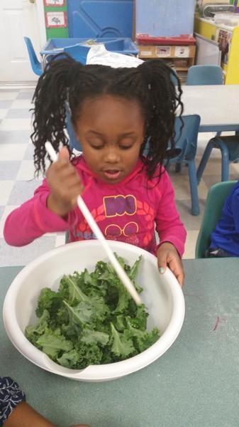 A young child stirs kale in a large white bowl.