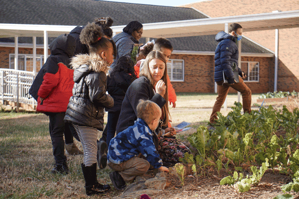 A teacher and students crouch down to look at plants growing in a garden.