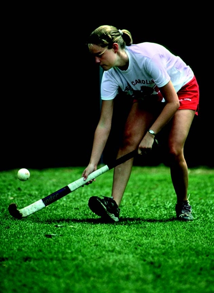 Decorative image of a young person playing field hockey on green turfgrass