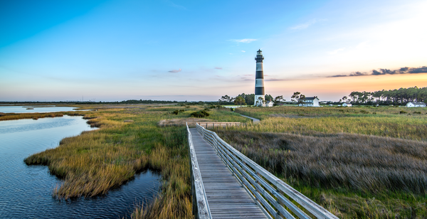 Bodie Island Lighthouse at sunset with a boardwalk leading to it in the foreground.