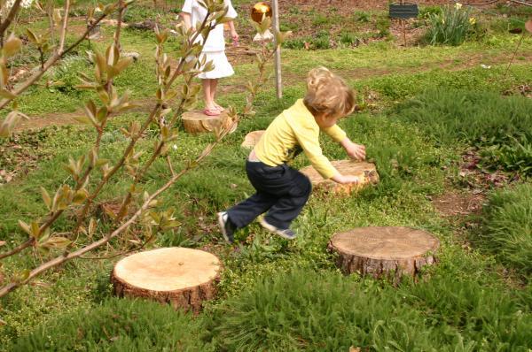 A child hops between smooth, flat tree trunks in garden