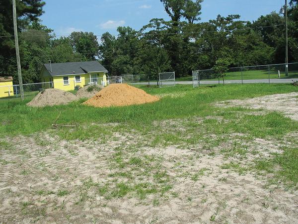 3 large dirt piles in grass in front of yellow house