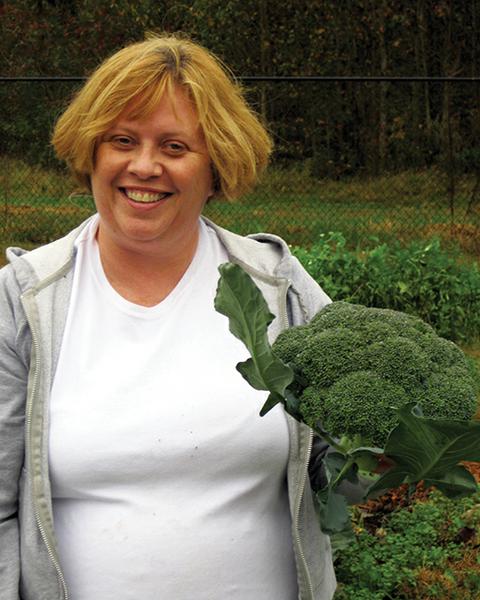 Person holding broccoli and standing in garden
