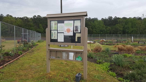 Weather-proof bulletin board in community garden with notices posted; cubbyholes underneath for pamphlets and other materials.