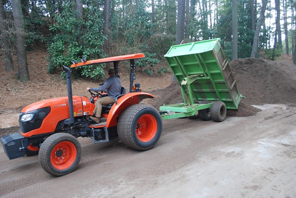 An orange tractor an a green dump trailer that is dumping out debris.