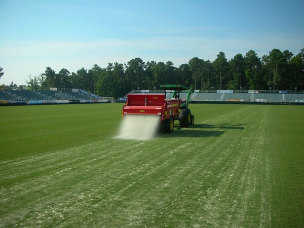 A tractor pulling equipment that is applying sand topdressing to an athletic field.