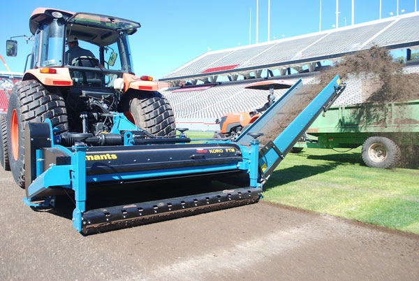 A tractor pulling a deep fraise mower that is expelling thatch into a collection trailer.