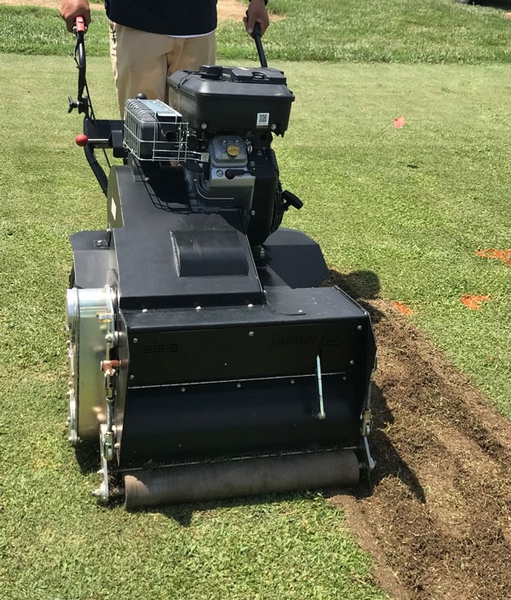 A person operates a walk-behind fraise mower on an athletic field.