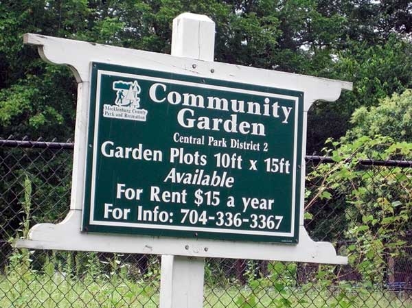 Wooden sign with name of garden, size of plots available, rental costs, and phone number.