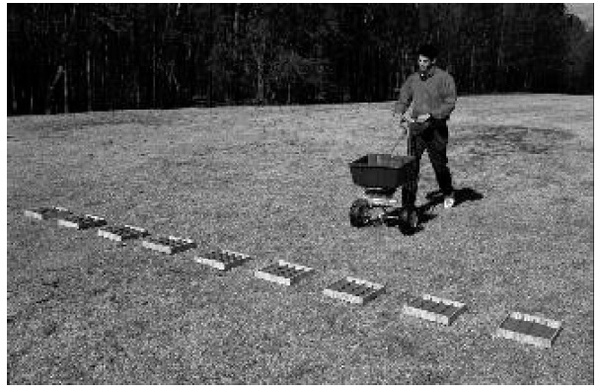 row of shallow boxes, trays, or pans on a line perpendicular to the spreader’s direction of travel.