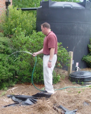 Man waters plants with hose, cistern in the background