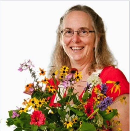 Lucy smiles wearing glasses and a red shirt, holding bouquet of flowers