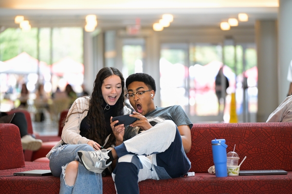 Two students looking at a phone with a surprised reaction