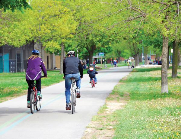 People cycle along a paved trail surrounded by trees