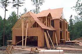 House frame with lumber piles on the ground and leaning against the house